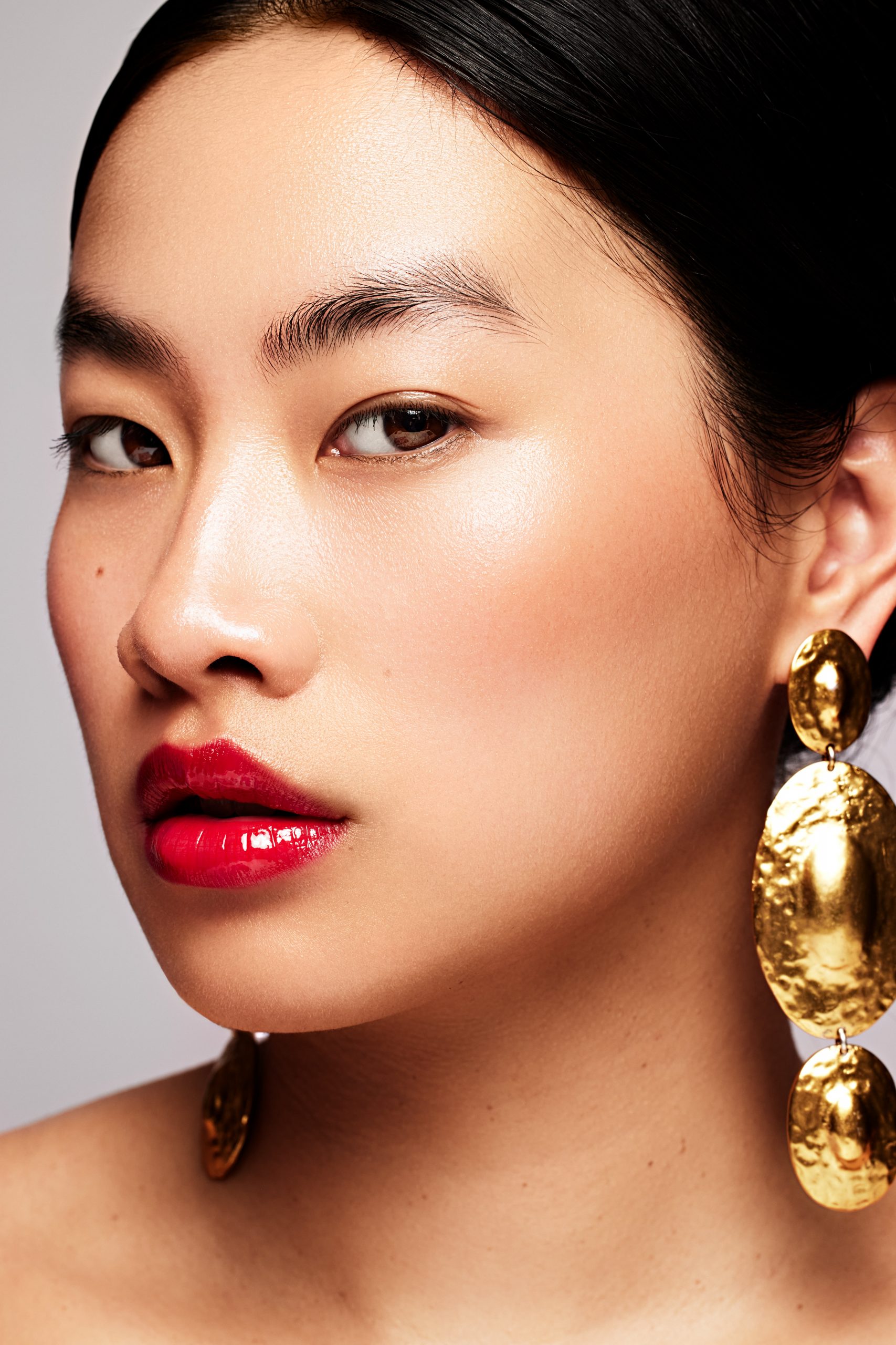 Beauty and jewelry portrait, model with bold red gloss lip and sculptural gold drop earrings, commercial beauty photography by Furkan Ramadani