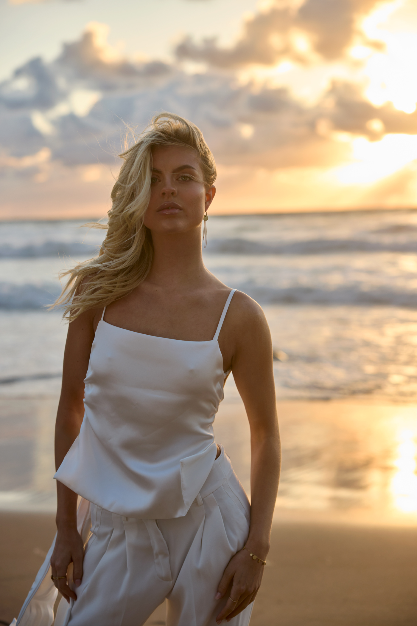 Full body fashion editorial Lisbon, model in white satin camisole and wide-leg trousers at sunset with ocean water reflection, photography by Furkan Ramadani