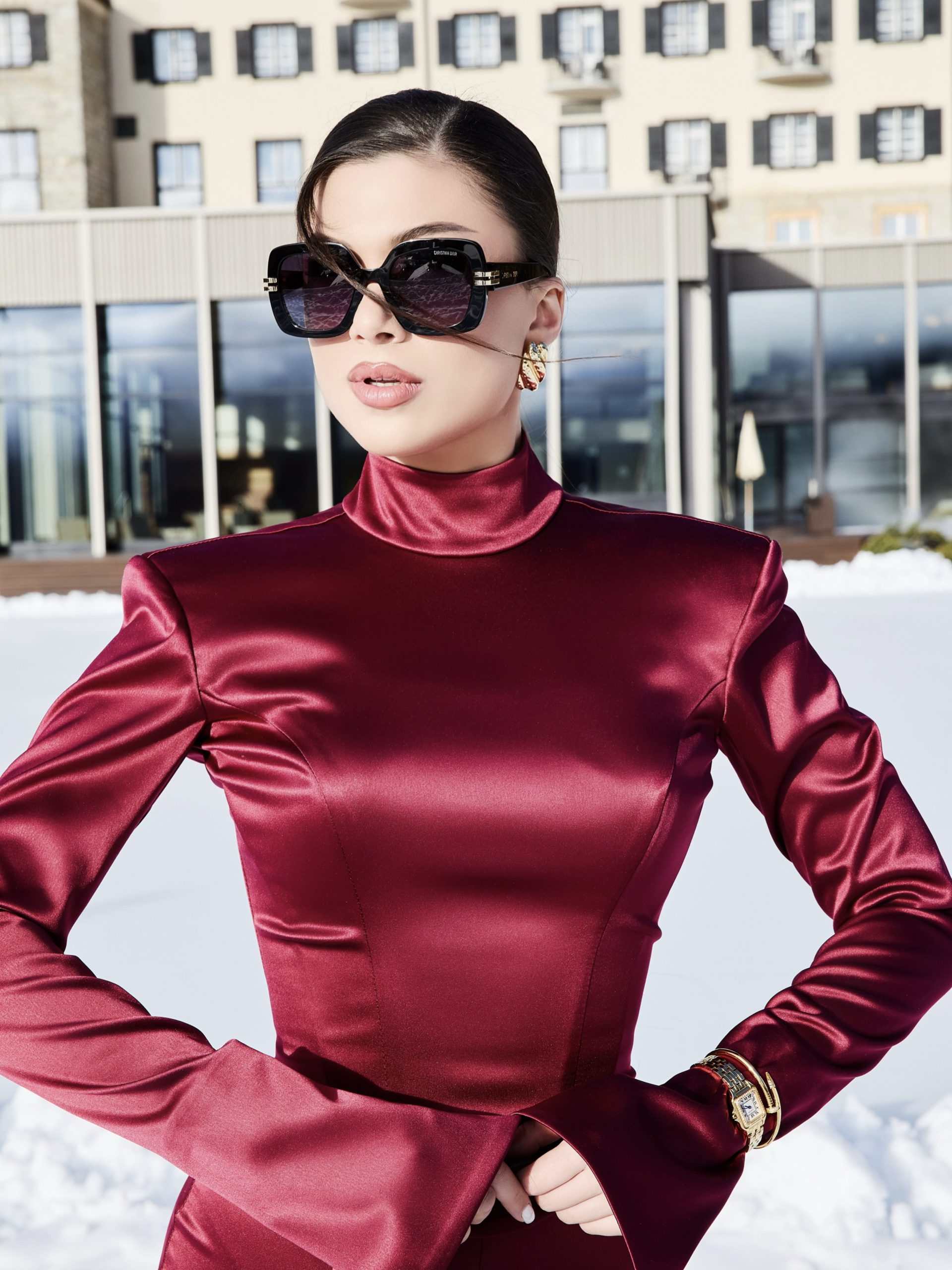Close-up beauty and fashion portrait, model in deep burgundy satin turtleneck with oversized sunglasses and Cartier watch, luxury hotel facade St. Moritz, photography by Furkan Ramadani