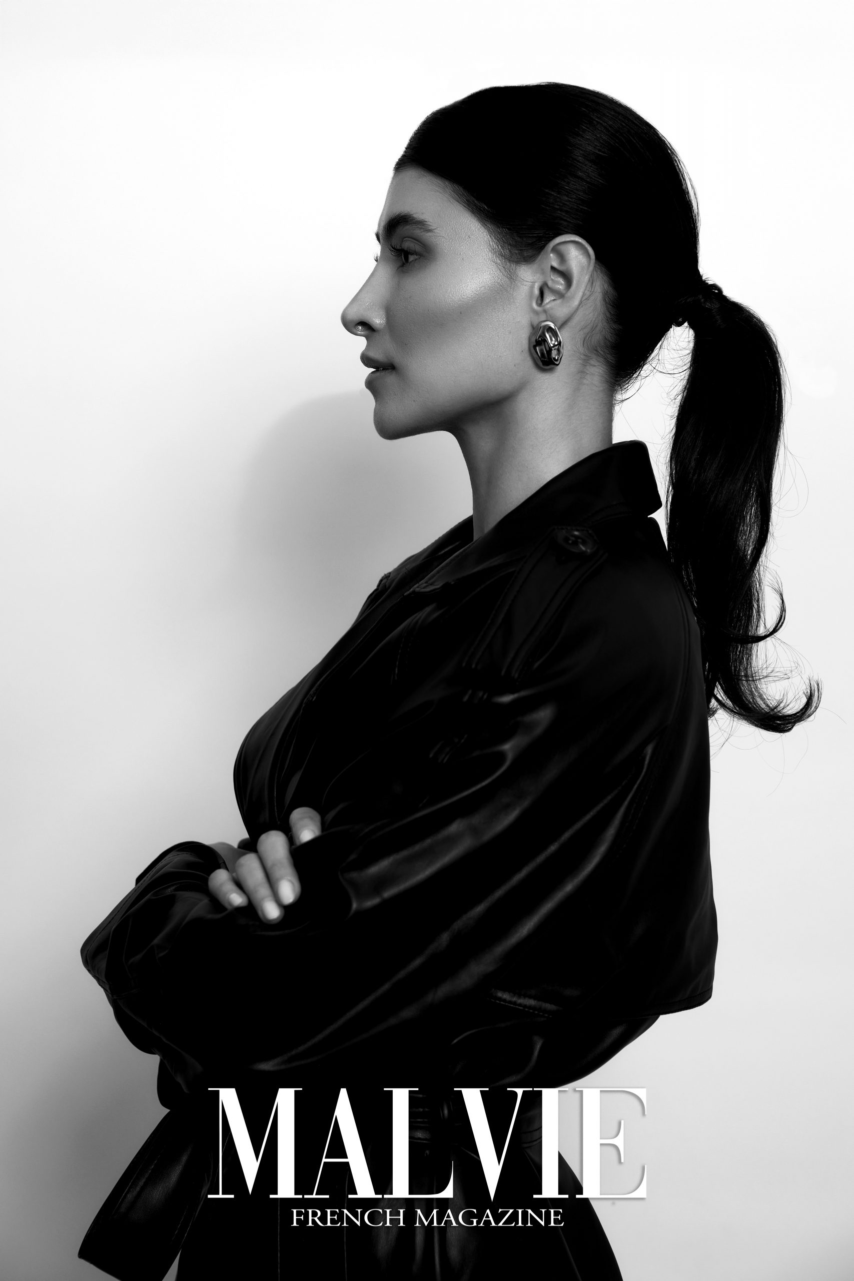 Black and white fashion portrait, model in black leather jacket side profile with sleek ponytail and arms crossed, published in Malvie French Magazine, photography by Furkan Ramadani