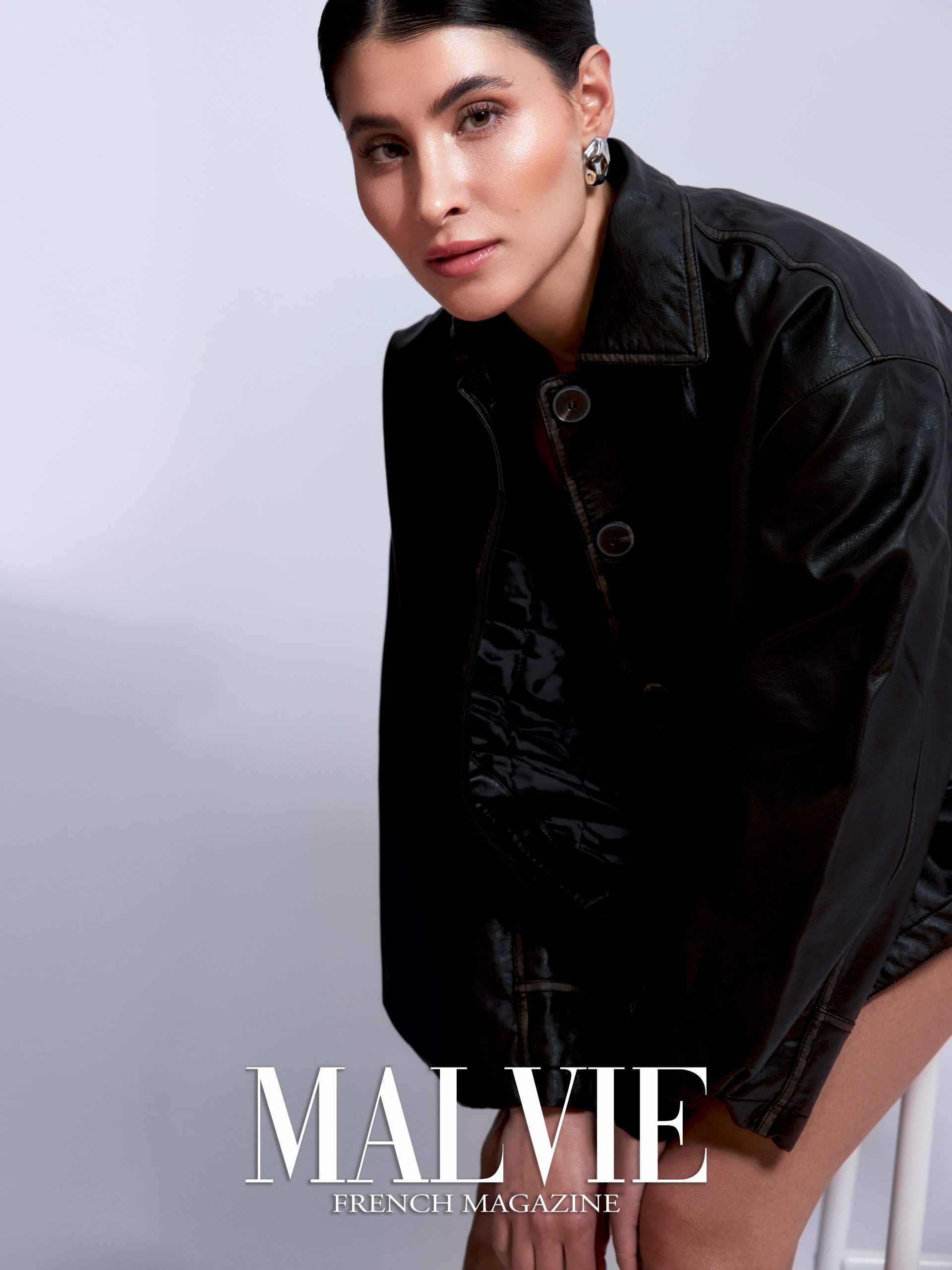 Fashion editorial, model in black leather jacket leaning toward camera with silver earring, soft studio light, published in Malvie French Magazine, photography by Furkan Ramadani